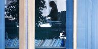 In einem Fenster sieht man den Umriss einer Frau an einem Schreibtisch