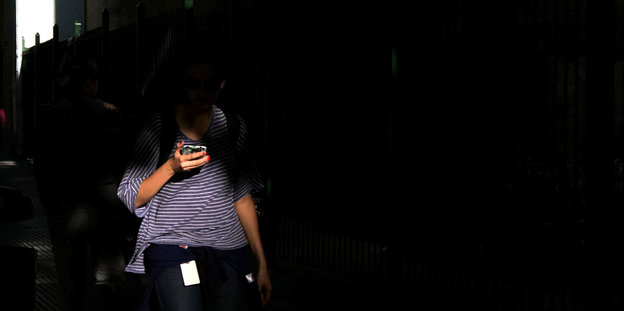 Eine Frau schaut auf das Display eines Handys, ihr Gesicht bleibt im Dunkeln