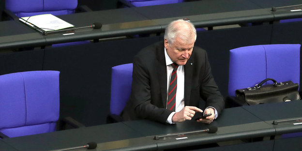 Horst Seehofer sitzt in den Sitzreihen des Bundestags und tippt auf seinem Smartphone