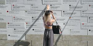 eine Frau fotografiert vor einer Wand mit Mauersteinen mit Beschriftung