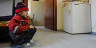Junge sitzt in Übergangswohnheim. Im Hintergrund ein Kühlschrank