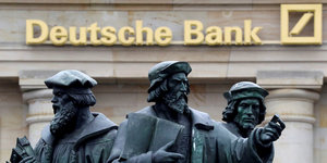 Drei Figuren stehen vor einem Gebäude, an dem Deutsche Bank steht