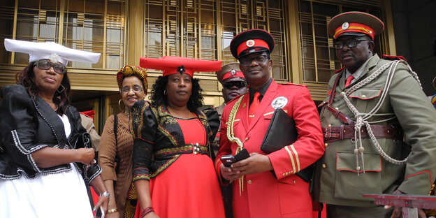 Drei schwarze Männer in Uniformen und drei schwarze Frauen in traditionellen Kleidern.