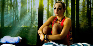 Ein geschminktes Mädchen sitzt vor einer Fototapete mit Waldmotiv. Sie sieht verweint aus