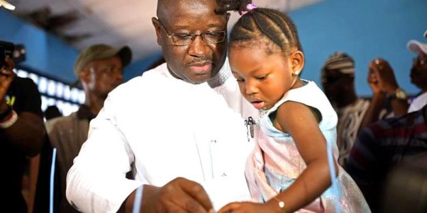 Der Gewinner der Wahlen in Sierra Leone gibt mit einem kleinen Mädchen auf dem Arm seine Stimme in eine Wahlurne ab