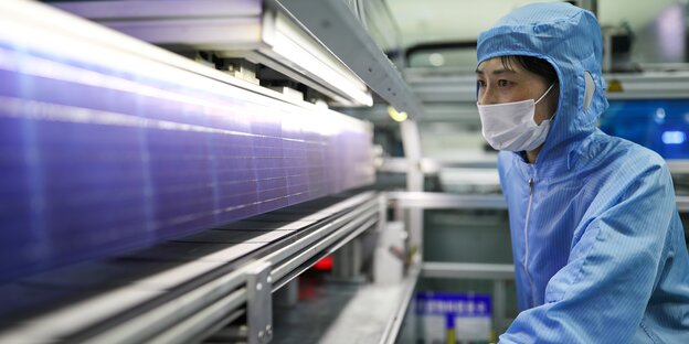 Chinesische Mitarbeiterin mit Schutzkleidung in Solarfabrik in China starrt konzentriert auf ein Solarpanel