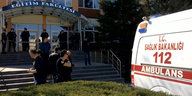 Ein Krankenwagen vor einem Institutsgebäude einer Universität, vereinzelte Polizisten und andere Menschen