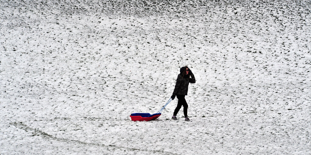 Eine Frau mit einem Schlitten geht über eine schneebedeckte Wiese.