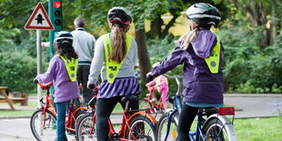 drei Kinder auf Fahrrädern stehen an einer kleinen Ampel