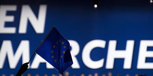 Jemand hält eine Europafahne vor einem En-Marche-Banner
