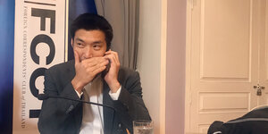 Juanggroongruangkit sitzt an einem Tisch und telefoniert per Handy; seinen Mund verdeckt er mit seiner Hand