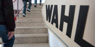 Männer gehen vor Wahl-Schild Treppe hoch