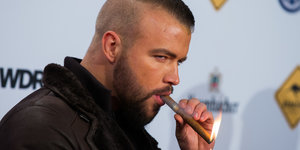 Der Rapper Kollegah zündet sich eine Zigarre an
