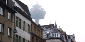 Eine Hausfront, dahinter ragt ein Funkturm im Nebel auf