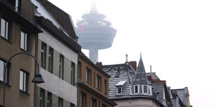 Eine Hausfront, dahinter ragt ein Funkturm im Nebel auf