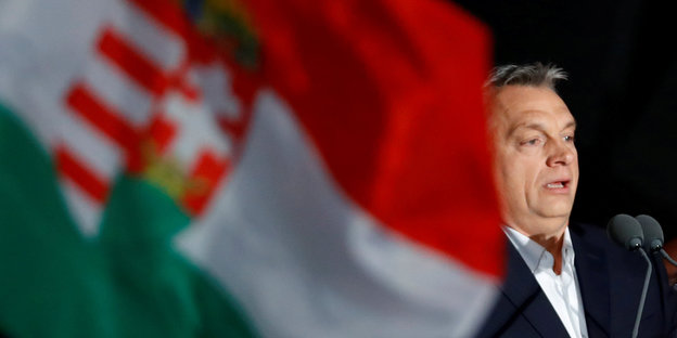 Viktor Orbán, neben ihm eine Ungarnflagge mit Wappen