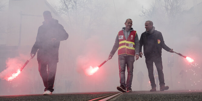 Drei Männer halten im Nebel bengalisches Feuer in ihren Hänen