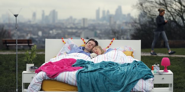 Zwei Menschen liegen aneinandergekuschelt in einem Bett, das unter freiem Himmel steht