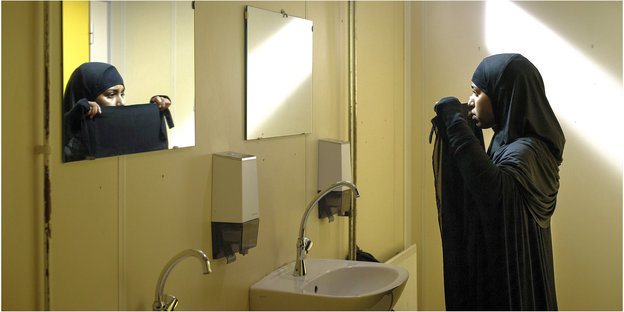 Eine Frau blickt in den Spiegel während sie ihren Gesichtsschleier anlegt
