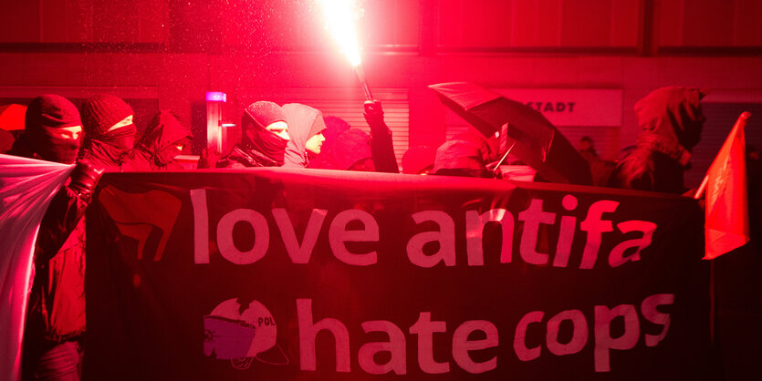 Schwarz gekleidete und vermummte Demonstranten tragen ein Transparent mit der Aufschrift "love antifa, hate cops".