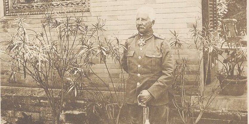 Ein alter Mann in Uniform. Um den Hals trägt er ein Eisernes Kreuz, in der Hand hält er einen Säbel.