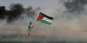 Ein Mann hält eine palästinensische Fahne hoch. Im Hintergund dichter Rauch