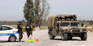 Soldaten stehen neben einem Polizeiauto, daneben steht ein Militärfahrzeug schräg auf einer Straße