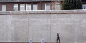 Ein Arbeiter eine hohe Mauer entlang, hinter der ein Haus und ein Baum zu sehen sind