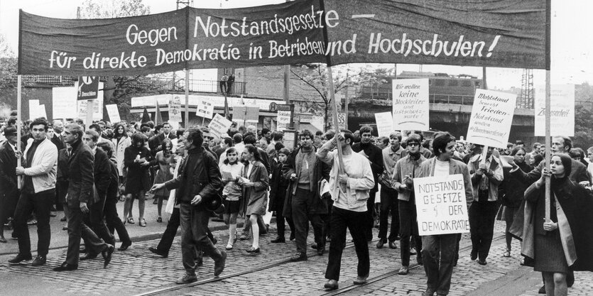 Schwarzweiß-Foto: Viele Menschen unter einem großen, in die Höhe gehaltenen Banner