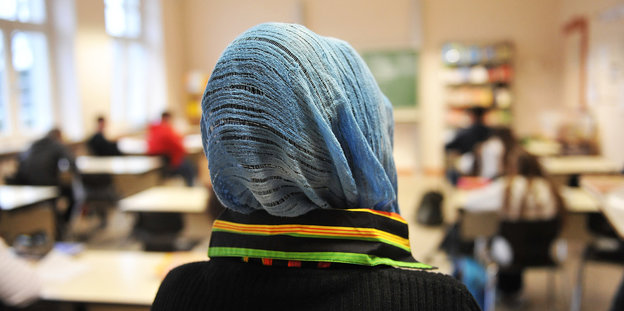 Ein Mädchen mit Kopftuch steht in einer Schule vor einem Klassenzimmer