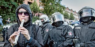 eine Demonstrantin spielt auf einer Blockflöte - dahinter behelmte Polizisten mit geschlossenem Visier