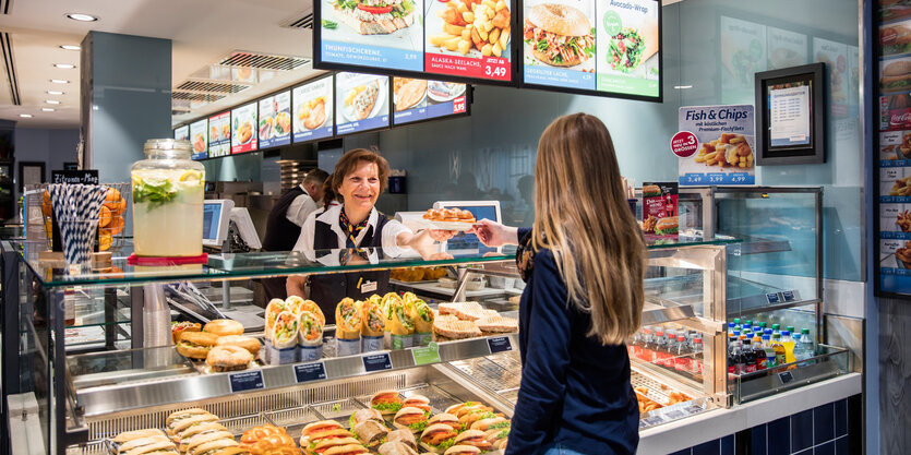 Eine Nordsee-Verkäuferin reicht einen Teller mit Brötchen über den Verkaufstresen.