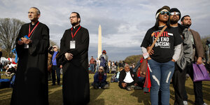 Zwei Pfarrer stehen links, ein Paar rechts. Eine Frau trägt ein T-Shirt mit der Aufschrift „United to End Racism“