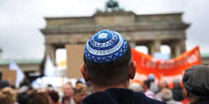 Ein Mann von hinten steht vor dem Brandenburger Tor in Berlin und trägt eine Kippa
