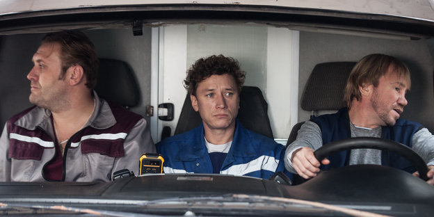 Drei Männer sitzen nebeneinander in einem Auto