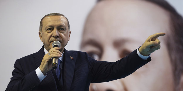 Recep Tayyip Erdoğan spricht in ein Mikrofon und zeigt mit der einen Hand zur Seite