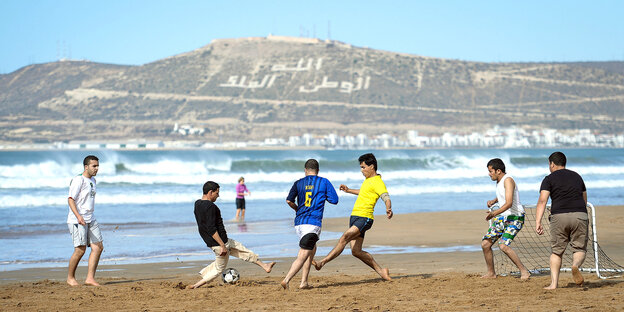 Sechs Männer spielen Fußball am Strand