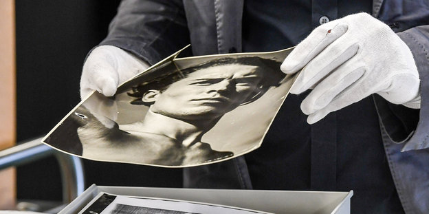 Zwei Hände in weißen Hanschuhen halten eine schwarz-weiß Fotografie
