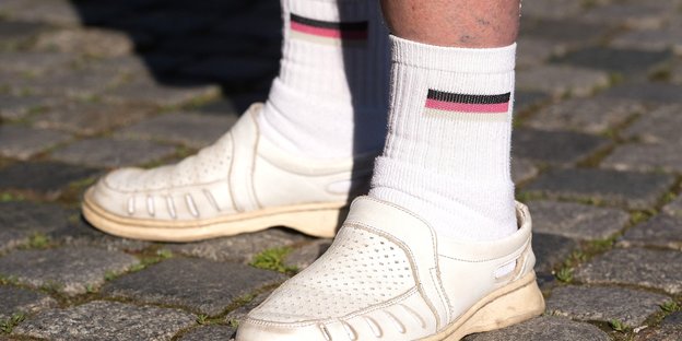 Jemand trägt weiße Socken mit aufgedruckter Deutschlandfahne in weißen Sandalen