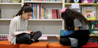 Zwei Mädchen sitzen vor einem Bücherregal und lesen.