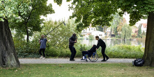 Ein Mann filmt einen Menschen in einem Rollstuhl im Park