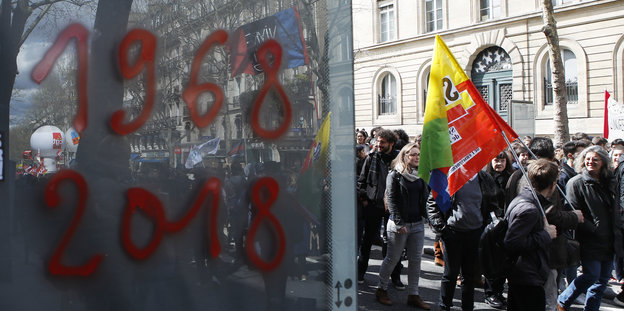 Menschen demonstrieren; daneben stehen auf eine Scheibe geschrieben zwei Jahreszahlen: 1968 und 2018