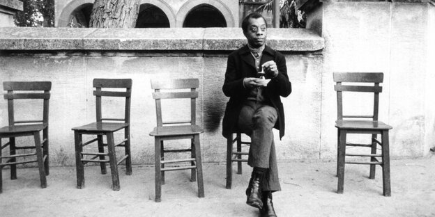 James Baldwin sitzt auf einem Stuhl, neben sich mehrere leere Stühle