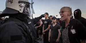 Polizisten mit Helm stehen vor schreiender Demonstrantin