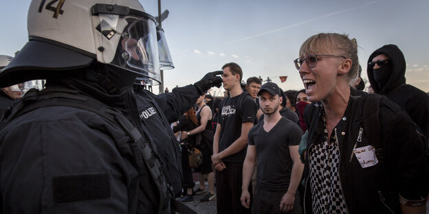 Polizisten mit Helm stehen vor schreiender Demonstrantin