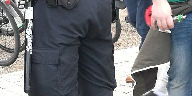 Ein Polizist hat am Gürtel einen Schlagstock mit einem Aufkleber "Spaß kostet" hängen.