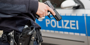 Ein Polizist mit gezückter Waffe vor einem Polizeiauto