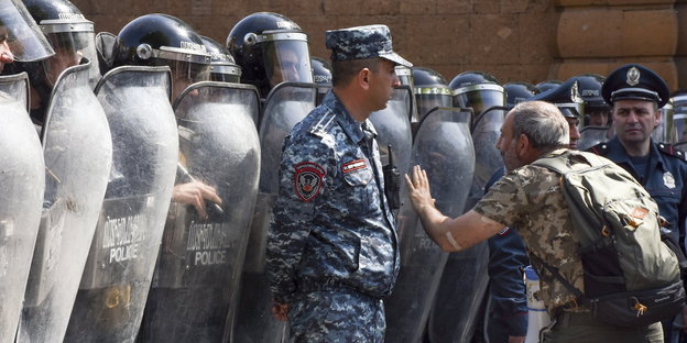 ein Mann vor einer Kette von Polizisten mit Helmen und Schildern