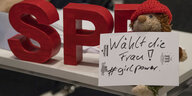 DIe Buchstaben SPD auf einem Tisch, davor ein Teddy und ein Zettel mit "Wählt die Frau! #girlpower"