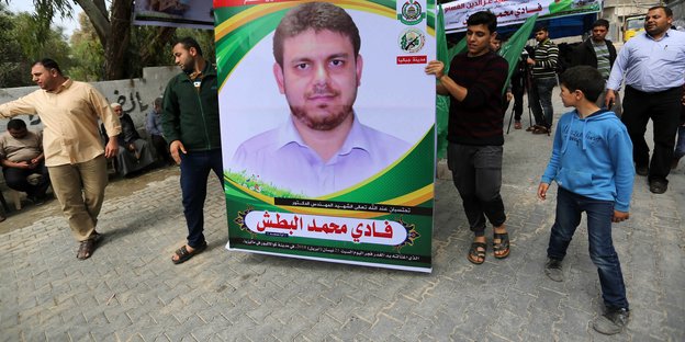 Zwei Männer halten ein Plakat mit einem Porträt von Fadi al-Batsch, daneben und dahinter mehrere Männer